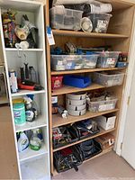 Photo of a white tall cabinet filled with cleaning products, oils, and tools on shelves.