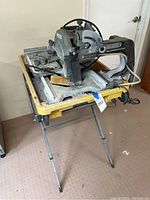 Side view of the Ridgid tile cutter mounted on yellow metal stand, showing legs and power cord.