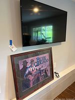 Samsung TV mounted on wall above the framed Blue Chicago art print lying against wall.