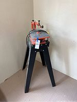 Overall view of the ScrollMate scroll saw on its black metal stand showing orange body and table top.