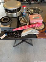 Table with all miscellaneous items seen from overview. Shows heater, beads box, clock, umbrella, slow cooker, cleaning spray, electronic devices, and cables.