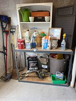 Shelf setup with assorted tools, gardening supplies, paint cans, and containers arranged on metal and wooden shelves.