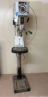 Full front view of Delta floor-standing drill press with base, column, table, head, and power cord