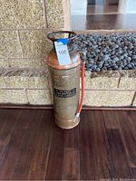 Front view showing copper fire extinguisher with embossed label and red hose attached.