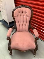 Front view of antique Victorian style pink upholstered wooden chair with carved wooden frame and tufted backrest.