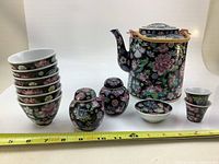 Front view of the tea set including the teapot, six tea cups stacked, two lidded jars, two small cups, and one bowl with a measuring tape