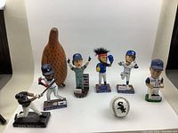 Front view of 6 baseball player bobbleheads, one white Sox baseball, and wooden carved item