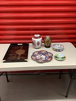 Photo showing six Japanese decorative items arranged on a table, including a lacquered tray, two vases, and three plates for overall lot perspective.