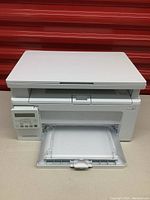 Front and top view of the HP LaserJet Pro MFP M130nw printer showing the paper tray open and scanner lid closed.