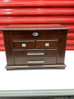 Closed wooden jewelry box with dark brown finish and metal knobs and handles on drawers