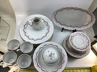 Top-down photo of the 43-piece JL Menau fine china set showing cups, plates, saucers, cream pitcher, covered dish, and large oval serving platter with floral and gold trim pattern.