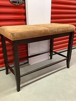 Side view of rectangular upholstered bench with dark wooden frame and tan cushioned seat showing minor wear.