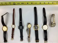 Top view showing all 7 watches lying flat in a row with a tape measure for scale.