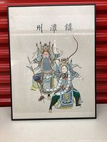Framed Asian artwork showing two warrior figures and Asian calligraphy, placed against a red background.