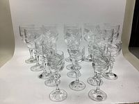 Front angled view displaying 16 clear vintage Bohemian crystal glasses in various shapes and sizes with cut glass decoration.