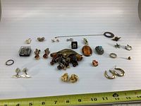 Top-down view of assorted vintage costume jewelry pieces arranged on a white background, featuring earrings, brooches, pins, rings, cufflinks, and a stick pin.