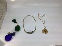 Two miniature perfume bottles and two vintage gold-tone necklaces displayed on a white surface.