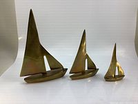 Three brass sail boats arranged largest to smallest on white background for size comparison and full view.