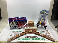 Photo of all 7 items including chess and checkers tins, poker chip set, Dominion card game, domino box, slinky, and boomerang with pouch.