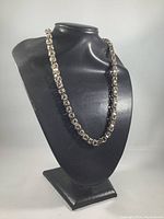 Front angled view of the vintage sterling silver Byzantine chain necklace displayed on a black stand showing full length and chain detail.