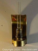 Front view of antique brass oil lamp showing glass chimney, brass burner, and reflector backplate.