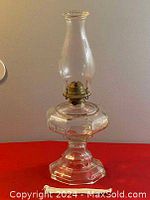 Full view of the antique oil lamp showing the glass body, brass burner, and tall chimney on a red surface.