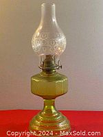 Full view of the oil lamp showing the yellow-green tinted glass reservoir and base, clear etched glass chimney, and brass burner assembly.
