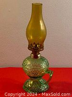 Side view of the assembled oil lamp with amber glass chimney atop the green cut glass base with a handle.