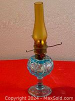 Image of full antique oil lamp on red surface, showing tall amber glass chimney and blue cut glass base.
