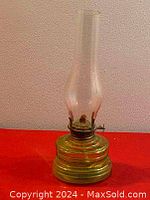 Full view of antique glass oil lamp showing its glass chimney and greenish base with concentric cut designs placed on red background.