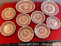 Nine Mason's ironstone plates in red transferware pattern displayed on red surface. Seven 8 inch side plates visible, along with one 11.25 inch oval service plate and one 10.5 inch round dinner plate.