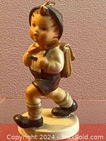 Porcelain figurine of a school boy from side angle showing details of clothing and posture.