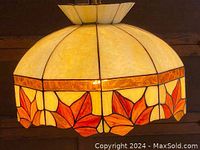 Full view of stained glass hanging lamp illuminated to show cream panels with orange leaf border and scalloped edge