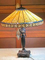 Full view of the Tiffany style stained glass table lamp lit, showing the yellow glass shade with brass metal inlay border and ornate base.