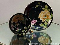 Side view of teacup and saucer showing floral design and glossy black background.