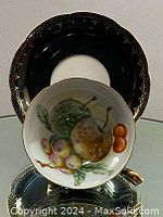 Front view of the saucer showing detailed hand painted fruit artwork on white base with black and gold trim