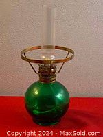 Side view of the vintage green glass oil lamp showing round green glass base, brass frame, and clear glass chimney.