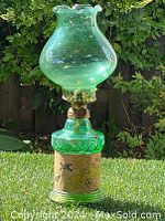 Full view of vintage green glass oil lamp outdoors, showing ruffled-top glass shade and decorated metallic band on base