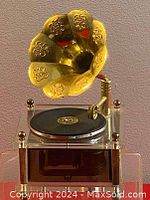 Front view of the miniature music box gramophone showing the gold-tone decorative horn and clear base with miniature record on the turntable.