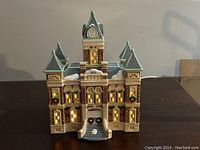 Front view showing detailed ceramic courthouse model lit internally with wreath decorations and snow accents.