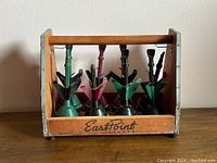 Full view of the wooden holder containing 8 lawn darts with green and burgundy fins, showing the East Point Sports logo.