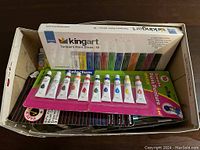 Box showing Kingart tempera paint sticks and Selectum gouache paint tubes still in packaging along with paint brushes.