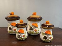 Set of four mushroom-themed ceramic canisters of varying heights with matching lids featuring mushroom knob tops placed together on flat surface.
