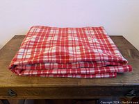 Folded wool blanket in red and white square plaid pattern placed on wooden surface