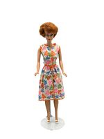 Full front view of the vintage 1960's Titian Bubble Cut Barbie doll wearing a sleeveless butterfly print dress with orange trim and white shoes standing on a display stand.