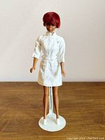 Front view of vintage 1969 Mattel Julia doll in original white nurse dress and shoes, standing on a white stand against a plain background.