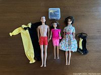 Three dolls and multiple clothing/accessories laid out on table showing all included items.
