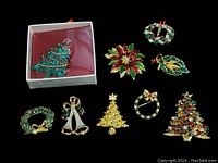 Photo showing the entire lot of 9 Christmas brooches arranged on black background with one brooch in a white box.