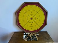 Full view of the Crokinole side of the octagonal wooden game board with yellow playing surface and scattered disks in black, white, and natural wood.