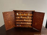 Open vintage thread spool cabinet showing four tilting shelves with scattered wooden spools inside.